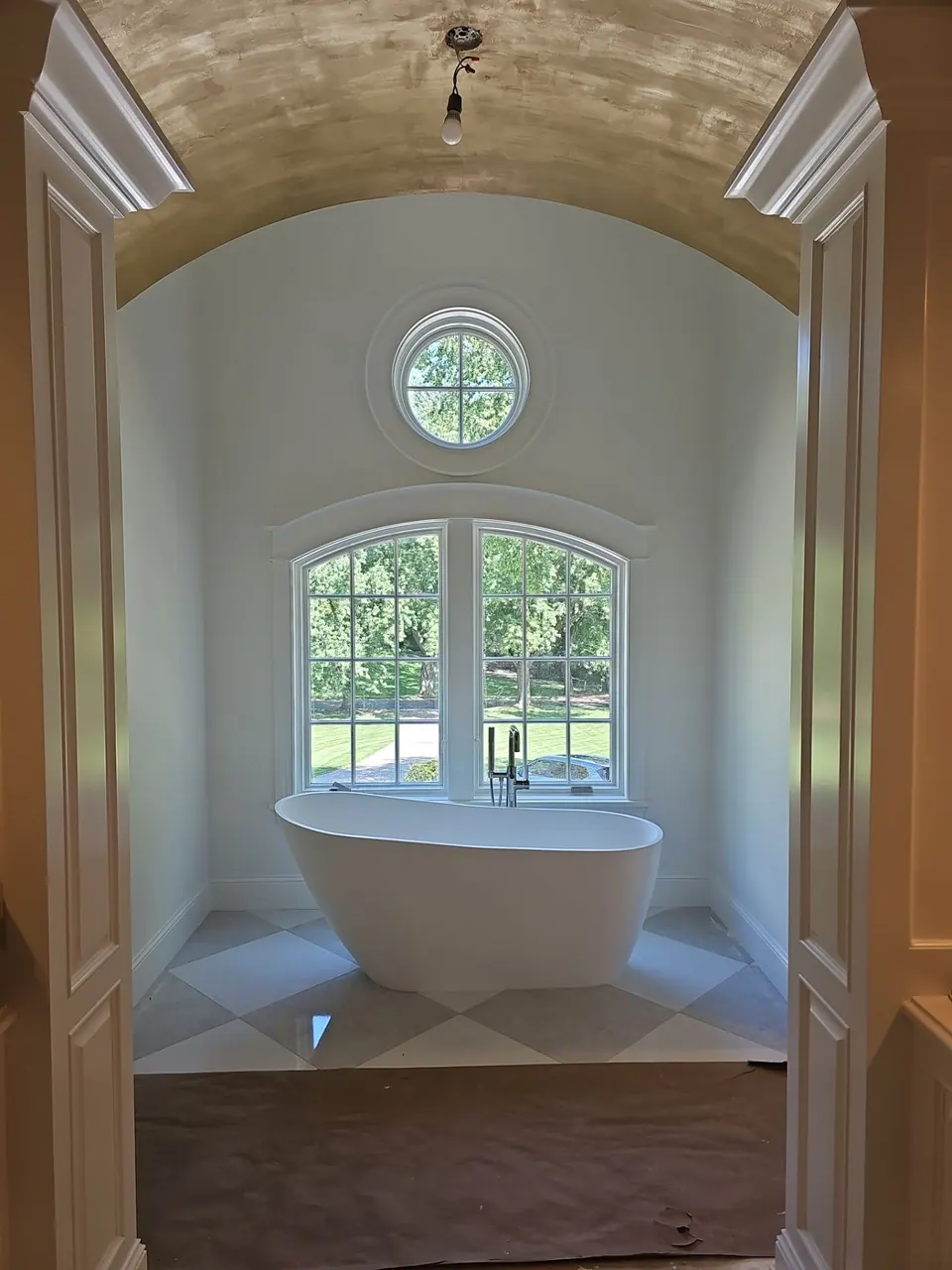 Arched bathtub nook with a round window, ceiling and trim painted white