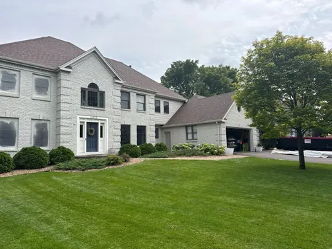 Two-story stucco home painted tan with white trim, photographed from the front yard.