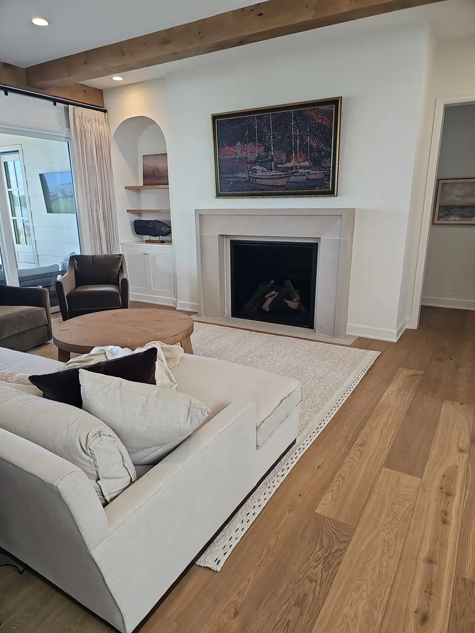 Living room with white walls, a plaster fireplace surround, an arched built-in nook, and exposed wood ceiling beams.